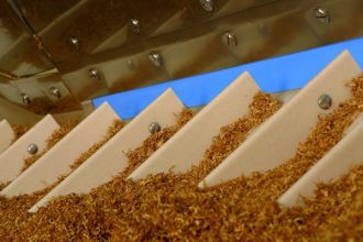Nahaufnahme von Zigaretten in der Produktion – Symbol für die globale Einflussnahme der Tabakindustrie.